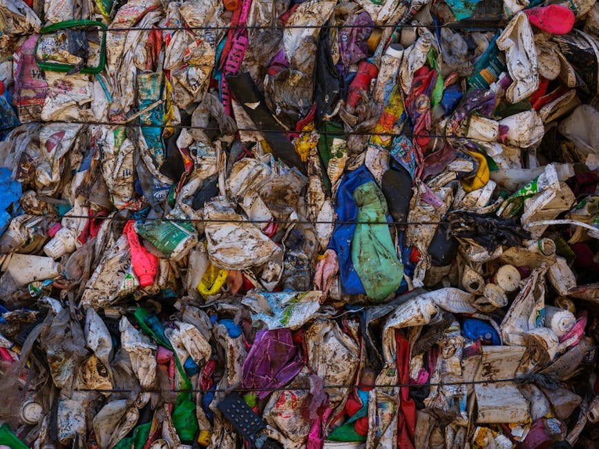 A collection of black woven plastic garbage bags, cardboard boxes, and plastic containers are piled up against an ornate, historical building with detailed stonework, arched windows, and iron grille d