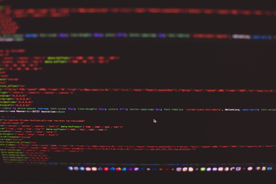 A person typing on a silver laptop with a black keyboard, situated on a wooden desk with a natural finish and visible grain pattern. The laptop screen displays lines of code in a dark-themed text edit
